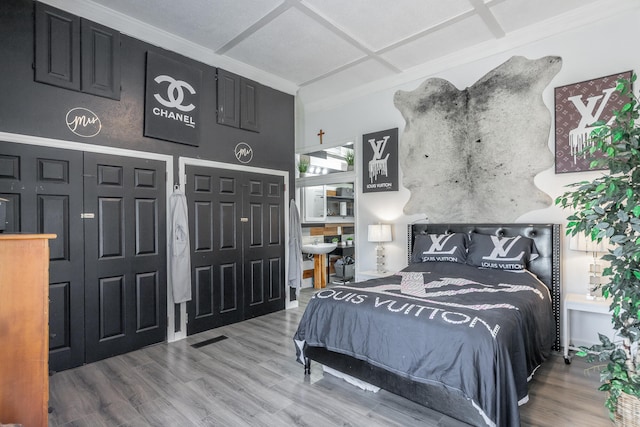 bedroom with wood-type flooring, two closets, ornamental molding, and coffered ceiling