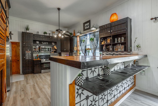 bar featuring dark brown cabinetry, stainless steel appliances, light hardwood / wood-style floors, and wood walls