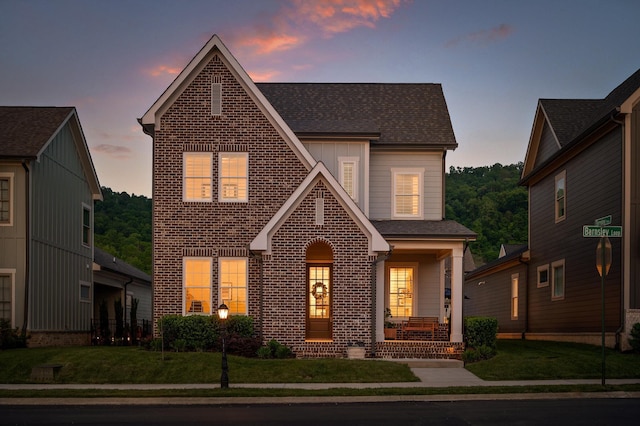 view of front facade featuring covered porch, brick siding, a shingled roof, and a front yard