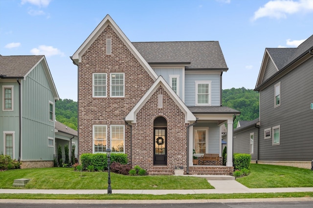 view of front of property featuring covered porch, a shingled roof, a front yard, and brick siding