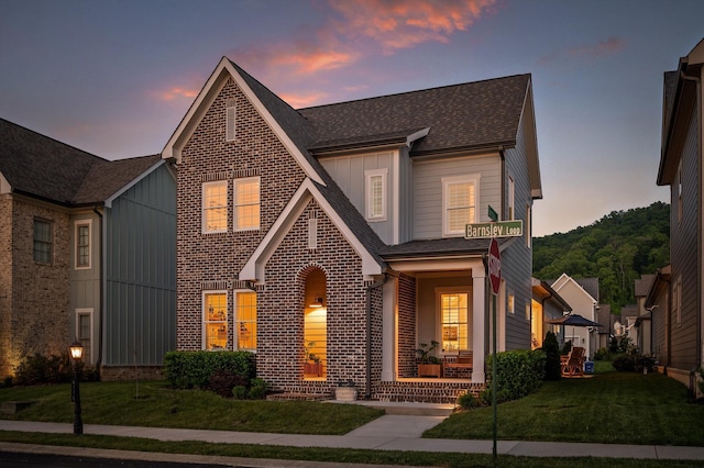 view of front of house featuring board and batten siding, a yard, a porch, and brick siding