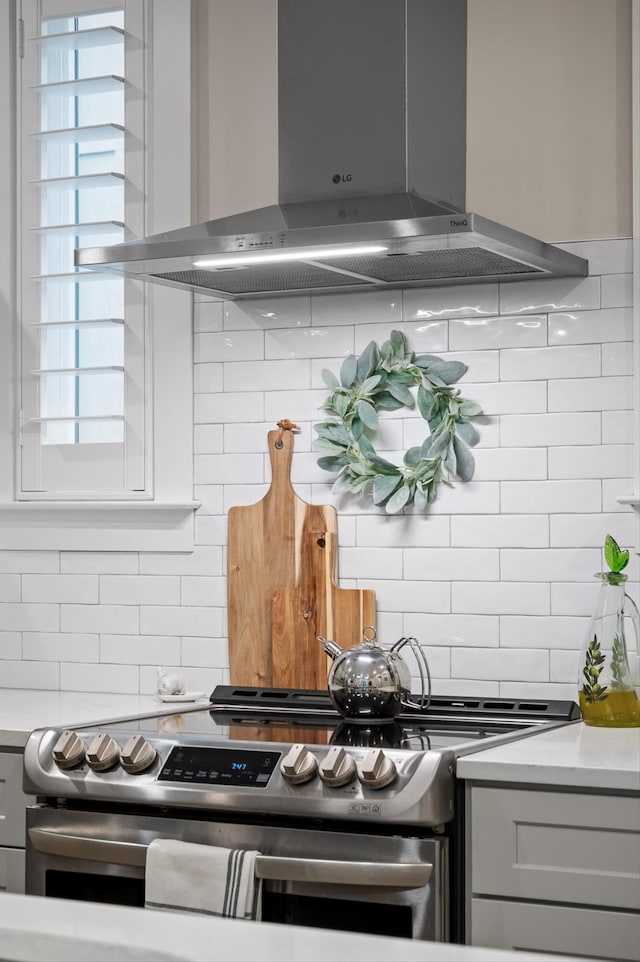 kitchen featuring light countertops, wall chimney exhaust hood, stainless steel electric range, and backsplash
