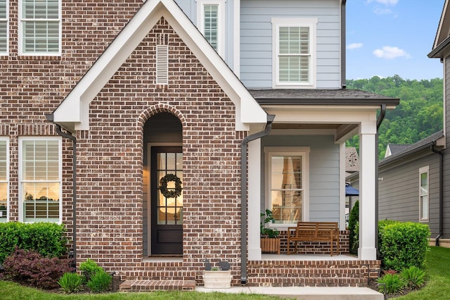view of exterior entry featuring brick siding and a porch