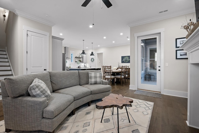 living area featuring ceiling fan, dark wood-style flooring, visible vents, stairway, and ornamental molding