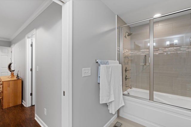 bathroom featuring shower / bath combination with glass door, wood finished floors, visible vents, crown molding, and baseboards