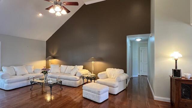 living area featuring wood finished floors, baseboards, ceiling fan, and high vaulted ceiling