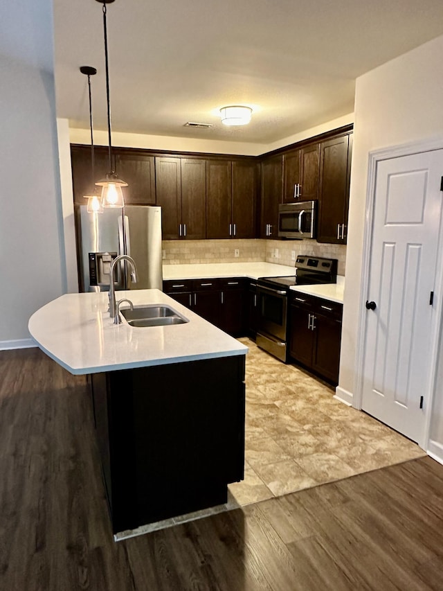 kitchen with sink, hanging light fixtures, light hardwood / wood-style flooring, an island with sink, and stainless steel appliances