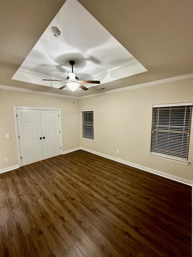 unfurnished bedroom with ornamental molding, a tray ceiling, ceiling fan, and dark wood-type flooring