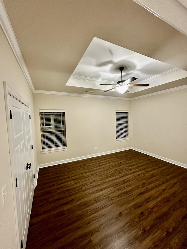 spare room featuring dark hardwood / wood-style floors, ceiling fan, ornamental molding, and a tray ceiling