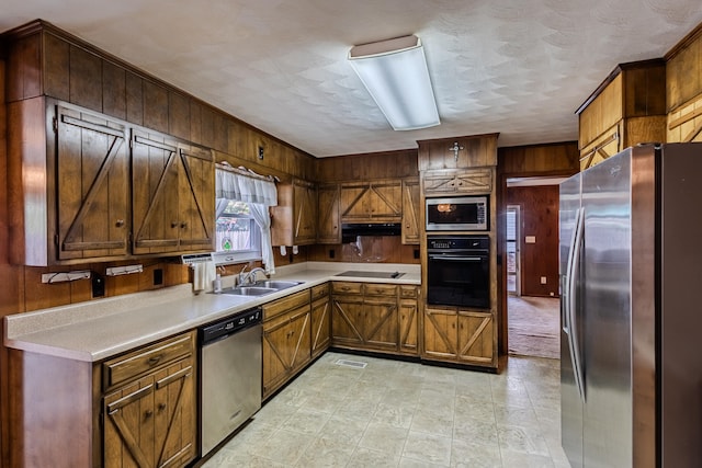 kitchen featuring sink, a textured ceiling, wood walls, and black appliances