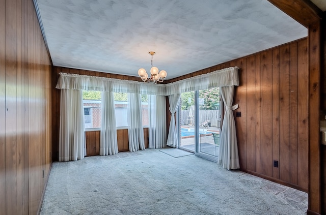 carpeted spare room featuring wooden walls and an inviting chandelier