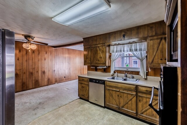 kitchen featuring light colored carpet, stainless steel appliances, ceiling fan, wooden walls, and sink