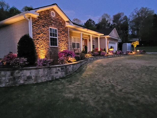 view of front of home with stone siding, a porch, a front yard, and a garage