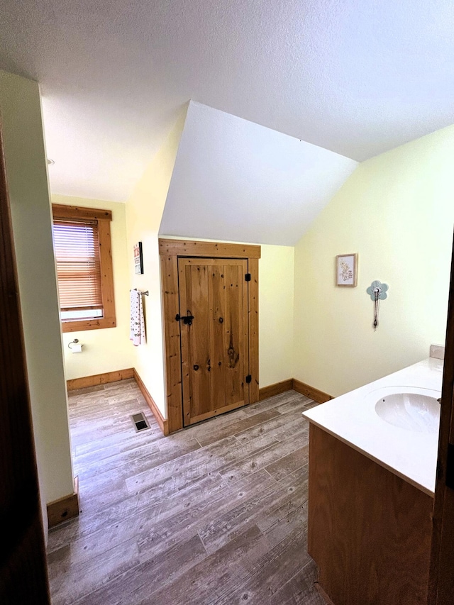 bathroom with hardwood / wood-style floors, a textured ceiling, and lofted ceiling