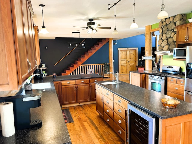 kitchen with sink, beverage cooler, light hardwood / wood-style flooring, an island with sink, and appliances with stainless steel finishes