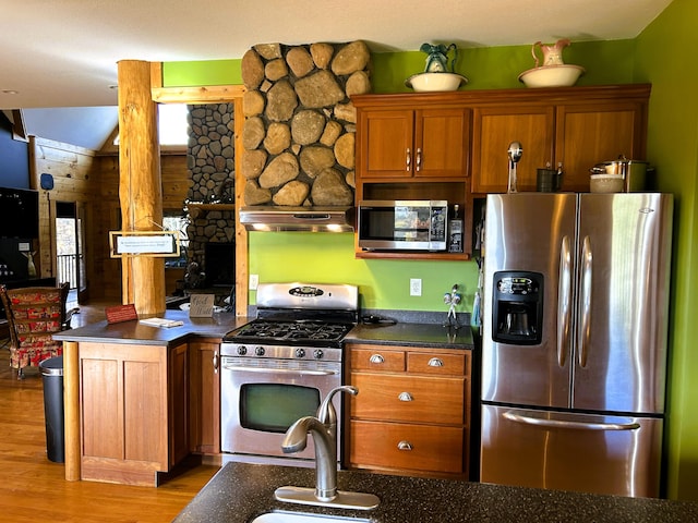 kitchen with wood walls, light wood-type flooring, stainless steel appliances, and exhaust hood