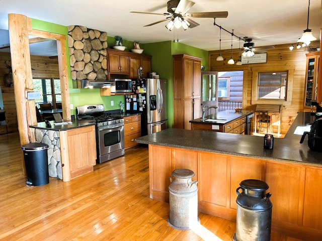 kitchen featuring light hardwood / wood-style flooring, kitchen peninsula, pendant lighting, wooden walls, and appliances with stainless steel finishes