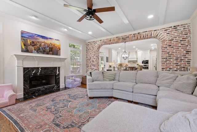 living room featuring a premium fireplace, beamed ceiling, ceiling fan with notable chandelier, and hardwood / wood-style flooring