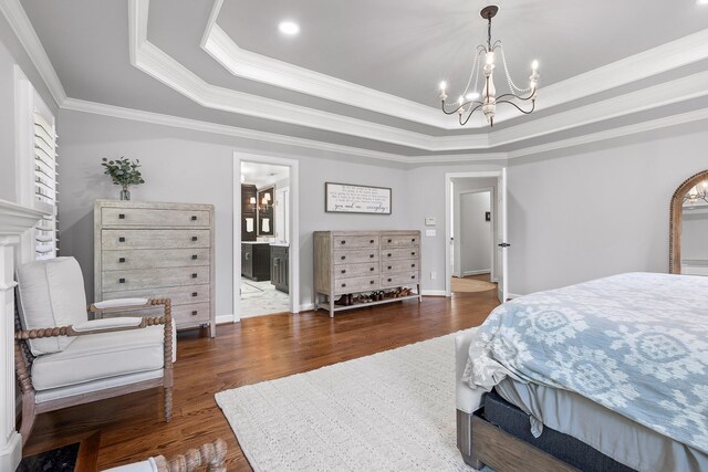 bedroom featuring dark hardwood / wood-style flooring, ensuite bath, a tray ceiling, crown molding, and a notable chandelier