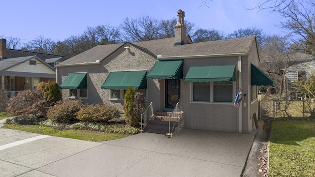 view of front of house featuring a chimney, stucco siding, a shingled roof, concrete driveway, and fence