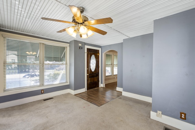 carpeted entrance foyer with visible vents, arched walkways, ceiling fan, and baseboards