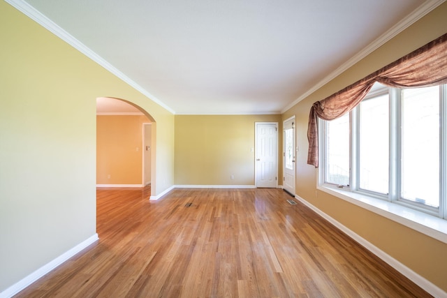 spare room featuring crown molding, arched walkways, light wood finished floors, and baseboards