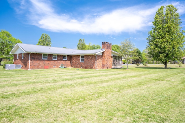rear view of property featuring brick siding, a lawn, a chimney, and metal roof