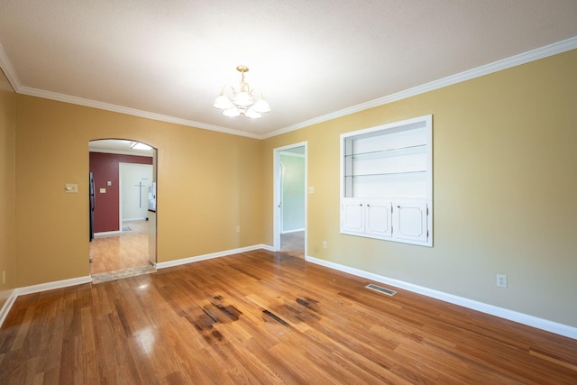 spare room featuring crown molding, arched walkways, a chandelier, built in shelves, and visible vents