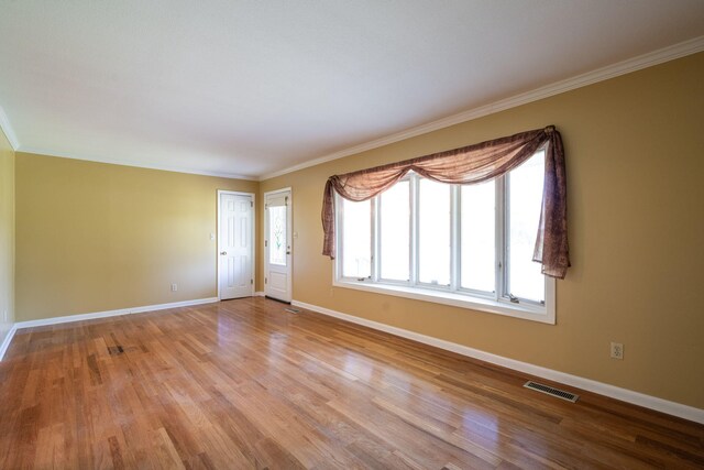 spare room featuring baseboards, visible vents, ornamental molding, and light wood finished floors