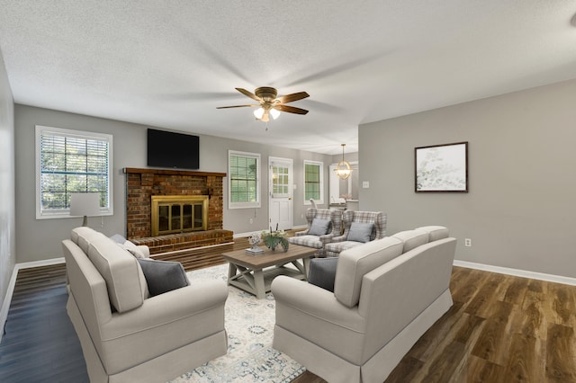 living room with ceiling fan, dark wood-type flooring, a textured ceiling, and a brick fireplace