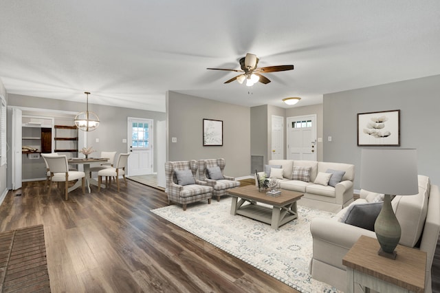 living room featuring ceiling fan with notable chandelier and dark wood-type flooring