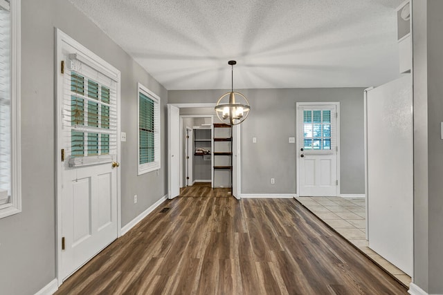 unfurnished dining area with a textured ceiling, a notable chandelier, and dark wood-type flooring