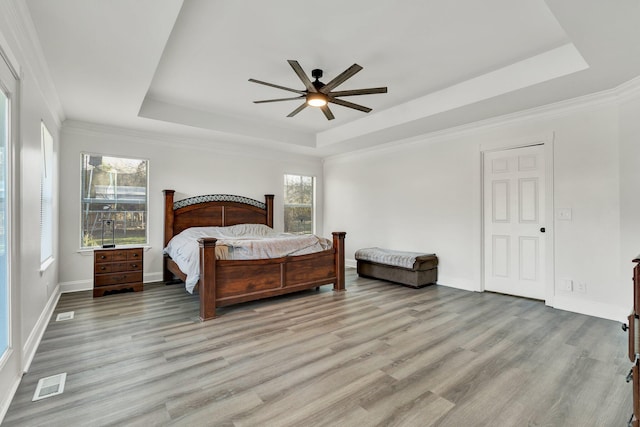 bedroom with crown molding, ceiling fan, a tray ceiling, and light wood-type flooring