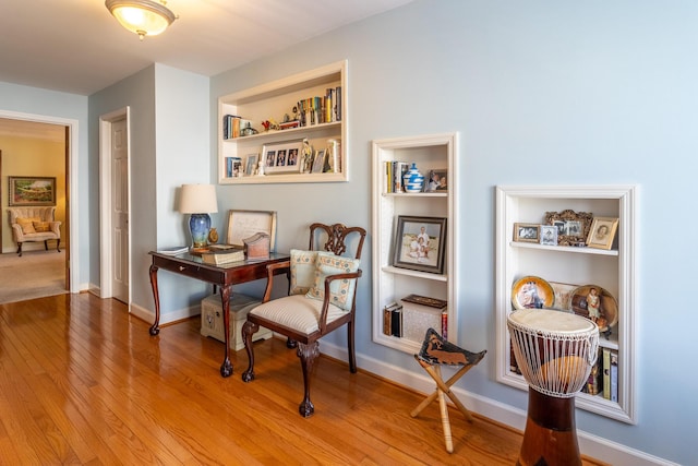 living area featuring built in shelves, wood finished floors, and baseboards