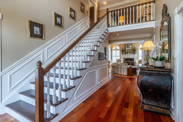 stairs with wood finished floors, ornamental molding, a fireplace, and a decorative wall