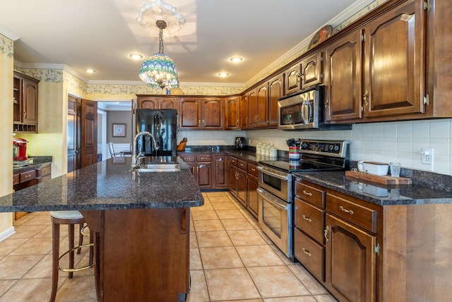 kitchen with a kitchen island with sink, a sink, appliances with stainless steel finishes, light tile patterned flooring, and decorative backsplash