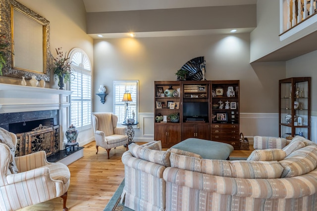 living area with light wood-style flooring, a fireplace, a high ceiling, and wainscoting