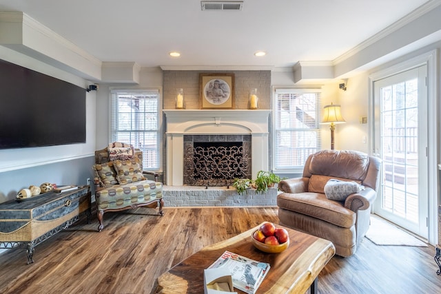 living area with wood finished floors, visible vents, a fireplace, recessed lighting, and crown molding