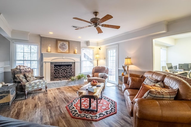living area with a fireplace, a healthy amount of sunlight, wood finished floors, and a ceiling fan
