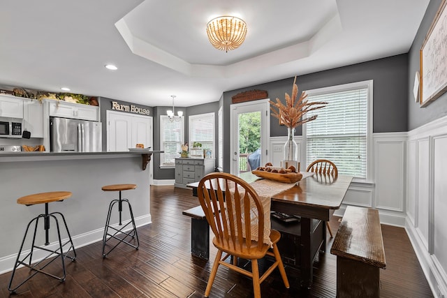 dining area with a tray ceiling, dark wood-type flooring, and an inviting chandelier