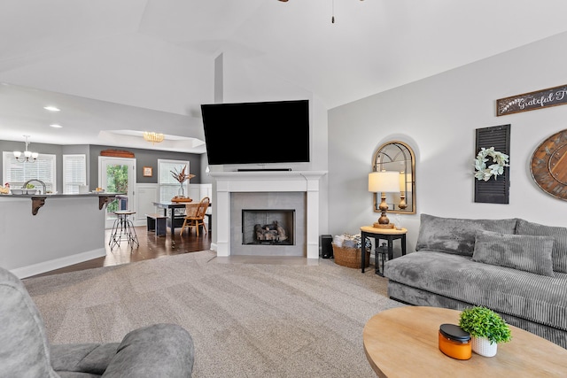 living room featuring ceiling fan with notable chandelier, lofted ceiling, and a tiled fireplace