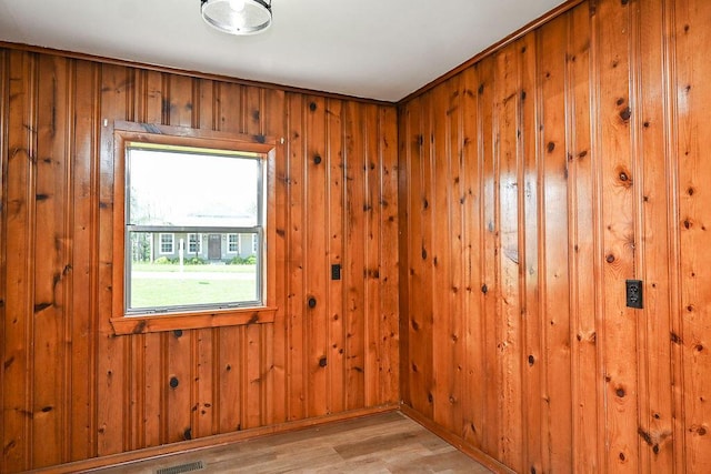 spare room with light wood-type flooring, wooden walls, and visible vents
