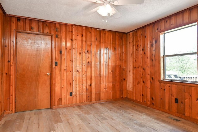 unfurnished room featuring wooden walls, a ceiling fan, visible vents, and wood finished floors