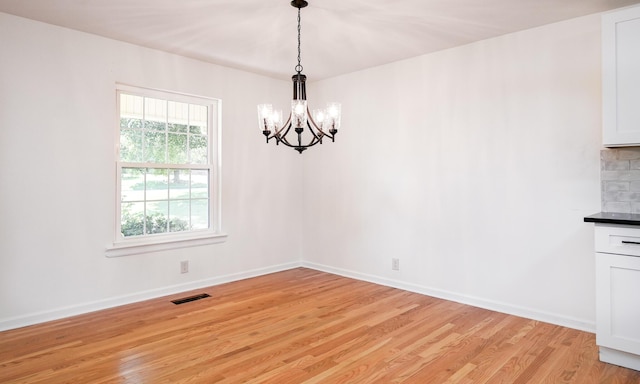 unfurnished dining area with an inviting chandelier, light hardwood / wood-style flooring, and a wealth of natural light