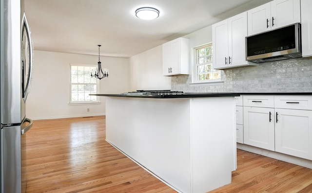 kitchen with appliances with stainless steel finishes, light hardwood / wood-style floors, a notable chandelier, white cabinetry, and decorative light fixtures