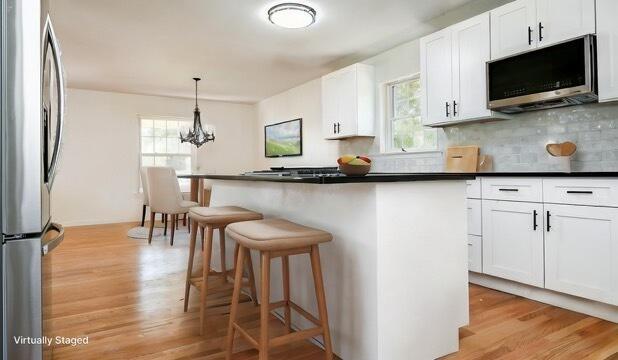 kitchen featuring white cabinets, an inviting chandelier, light wood-type flooring, a breakfast bar area, and appliances with stainless steel finishes