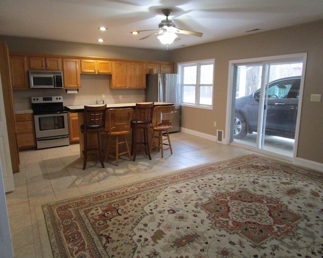 kitchen featuring a breakfast bar, ceiling fan, a kitchen island, stainless steel appliances, and light tile patterned flooring