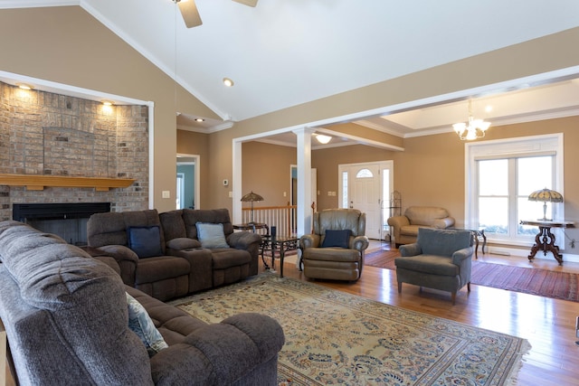 living room with crown molding, high vaulted ceiling, a brick fireplace, hardwood / wood-style flooring, and ceiling fan with notable chandelier