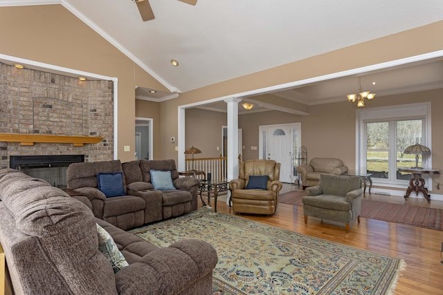 living room featuring crown molding, high vaulted ceiling, a brick fireplace, hardwood / wood-style flooring, and decorative columns