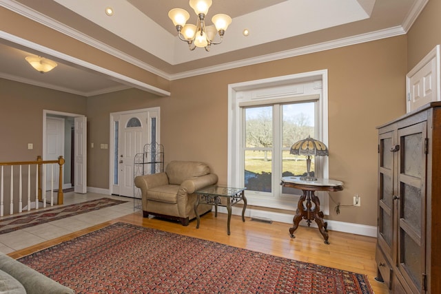 sitting room with hardwood / wood-style floors, a tray ceiling, ornamental molding, and a chandelier